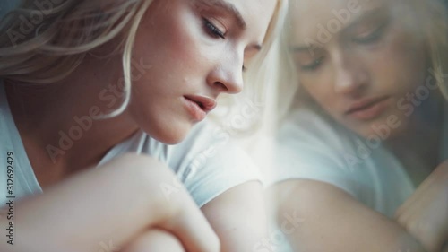 Close up face woman sits on the windowsill looks out the window frustration sickness hopeless loneliness depression alone beautiful home bed lonely gown comfortable slow motion