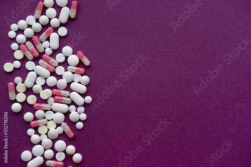 Pills and capsules on purple background from above. Copy space.