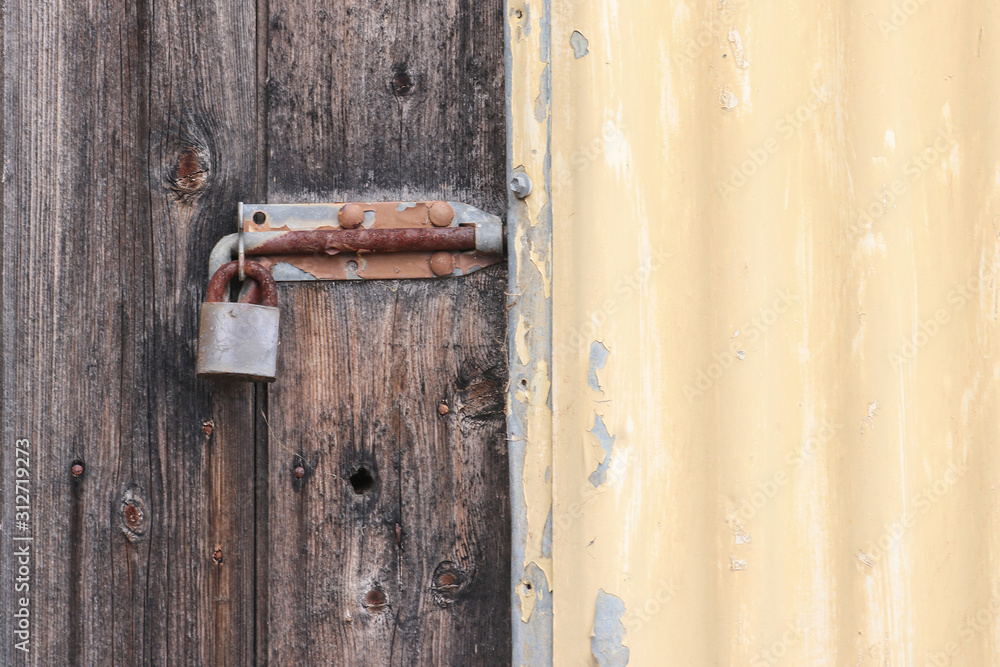 rusty padlocked bolt on old wooden door and painted corrugated iron shed