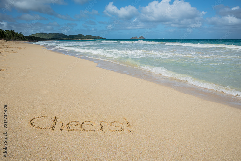 Fototapeta premium Cheers written in the sand on Waimanalo Beach in Hawaii with the ocean in the background