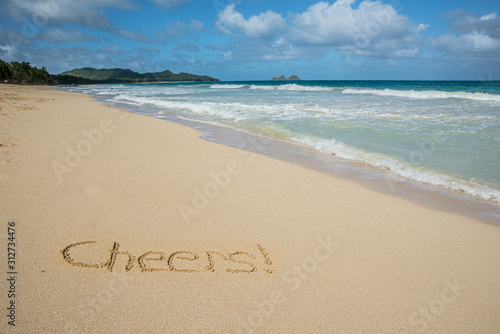 Cheers written in the sand on Waimanalo Beach in Hawaii with the ocean in the background