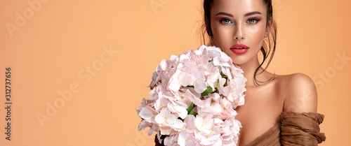 Beautiful white girl with flowers. Stunning brunette girl with big bouquet  of hydrangeas. Closeup face of young beautiful woman with a healthy clean skin. Pretty woman with bright makeup