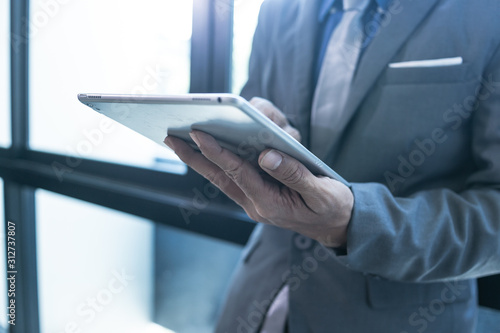 Businessman using tablet, standing near the window at office.