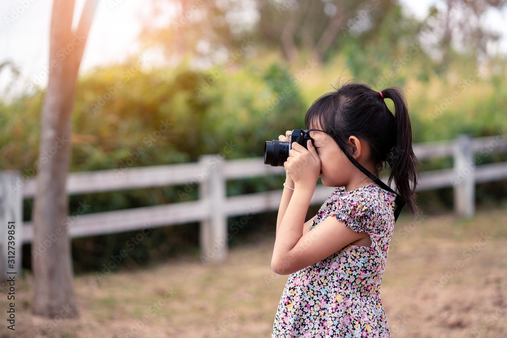Asian little child girl holding film camera and taking photo with of green natural background
