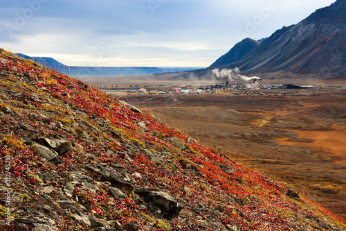 Arctic industrial landscape. View from the slope of the mountain, covered with autumn tundra, to the valley and a small industrial village. Smokestacks of a power plant. Egvekinot, Chukotka, Russia. photo