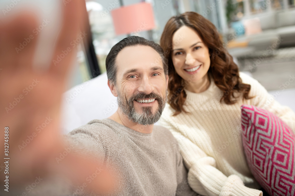 Smiling couple having good time in the furniture salon making selfie