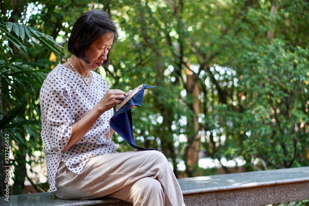 Fototapeta premium An old asian woman sitting on the bench embroidering handkerchief in the garden