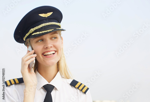 female pilot speaking on phone whilst at work wearing uniform. Young business woman speaking on the phone smiling 