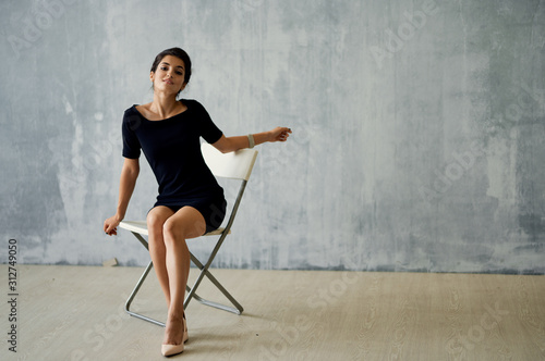 Bild auf Leinwand young woman in black dress sitting on a chair