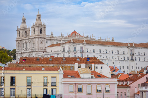 Colorful walls of the buildings of Lisbon, with orange roofs and the Church of Sao Vicente of Fora in the background. Sunny day and blue sky in summer. Travel and real estate concept. Lisbon, Portugal
