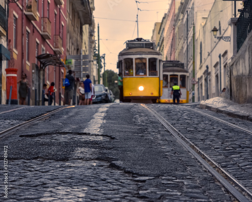 Travel concept of Lisbon famous trams. Focusing on the cobbled streets with the trams in the foreground. In the background, tourists and trams out of focus, in the light of the sunset. Lisbon, Portuga