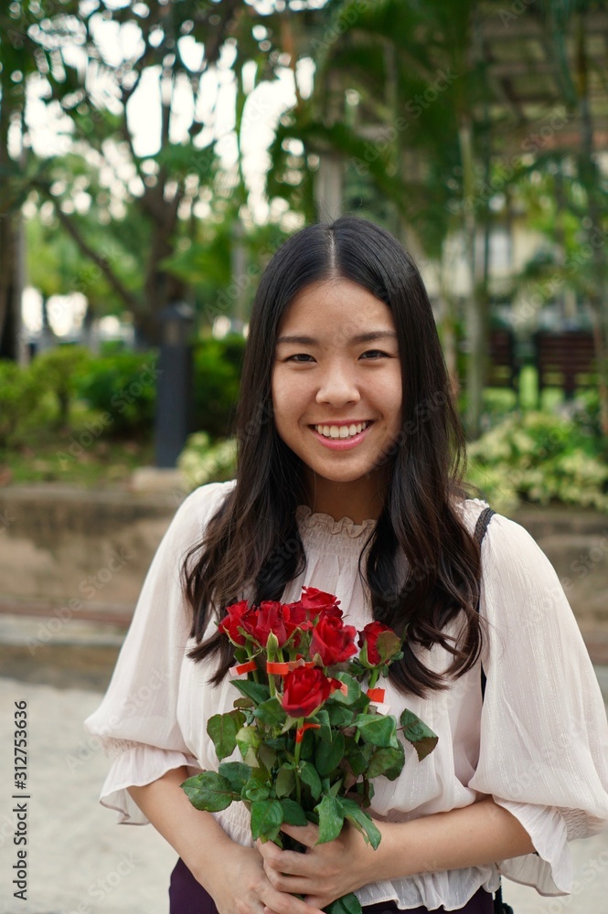 A young beautiful asian woman wearing white blouse holding a red rose bouquet in the garden A young beautiful asian woman wearing white blouse holding a red rose bouquet in the garden