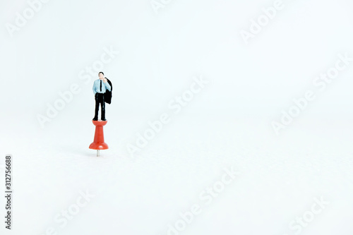 Miniature business concept - a businessman standing on a thumbtack / push pin with white background