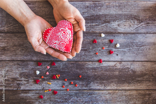 Valentine day gingerbread cookies heart in wooman hands with sprinkles on wooden background