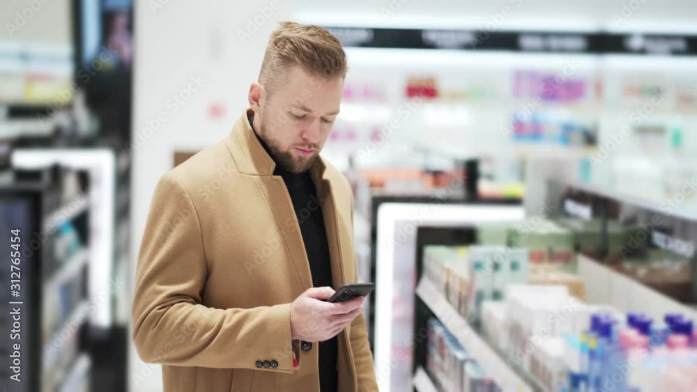 Young bearded man uses mobile phone and chatting online in shopping mall Young bearded man uses mobile phone and chatting online in shopping mall
