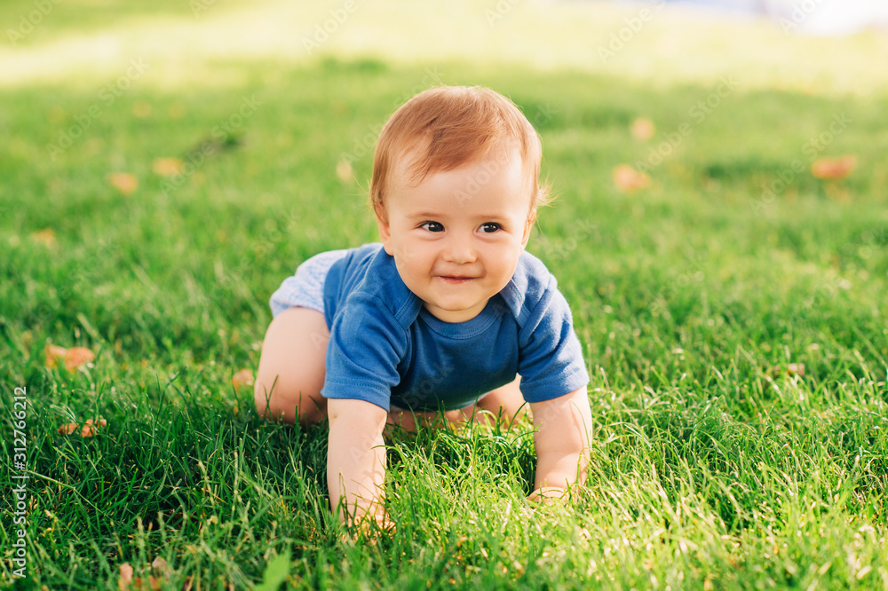 Adorable red haired baby boy crawling on fresh green grass in summer park - obrazy, fototapety, plakaty 