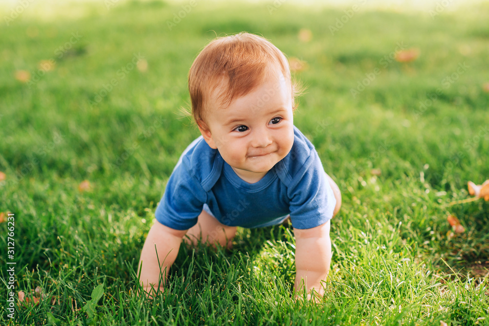 Adorable red haired baby boy crawling on fresh green grass in summer park Adorable red haired baby boy crawling on fresh green grass in summer park