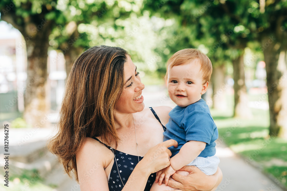 Fototapeta premium Outdoor portrait of happy mother holding adorable baby boy in arms