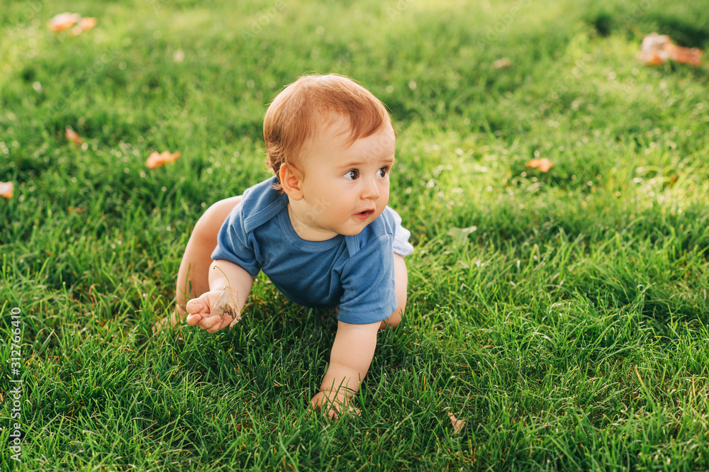 Adorable red haired baby boy crawling on fresh green grass in summer park Adorable red haired baby boy crawling on fresh green grass in summer park