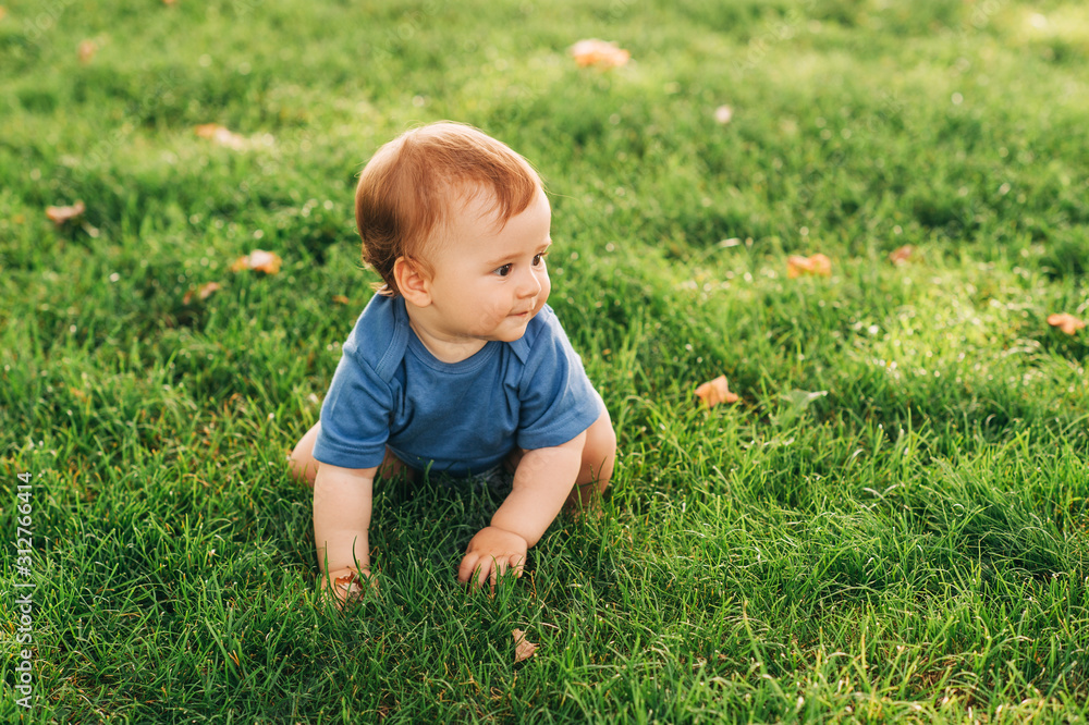 Adorable red haired baby boy crawling on fresh green grass in summer park Adorable red haired baby boy crawling on fresh green grass in summer park