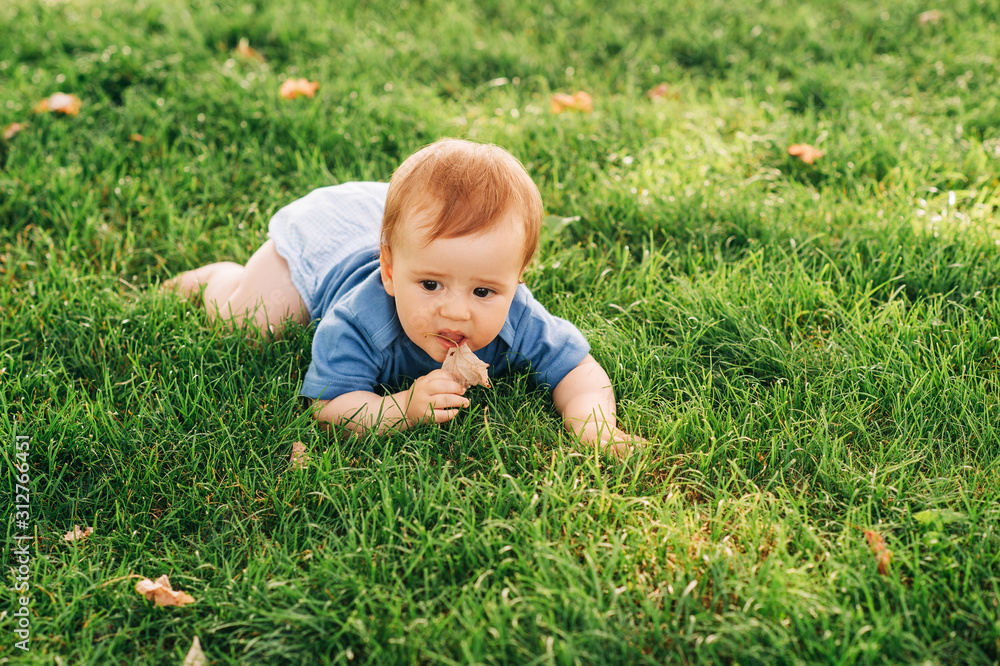 Adorable red haired baby boy crawling on fresh green grass in summer park, eating dry leaf Adorable red haired baby boy crawling on fresh green grass in summer park, eating dry leaf