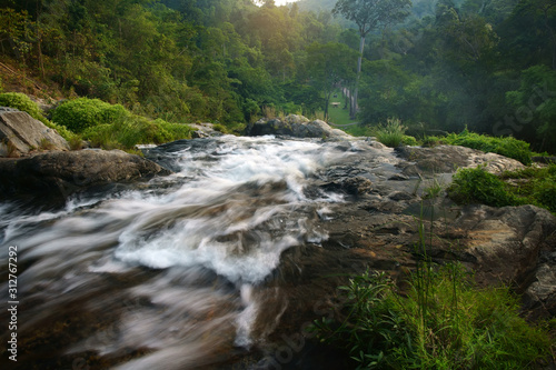 Fototapeta Naklejka Na Ścianę i Meble -  stream waterfall with rock or stone and tree in green jungle or forest with camping tent on winter holiday relax and vacation travel trekking and picnic on lawn or grass at Khlong Nam Lai Waterfall