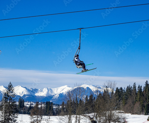 A chairlift with an unrecognizable skier on blue sky over Tatra mountains and a forest in Bialka ski resort in Poland