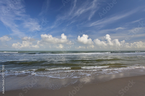 Fale na brzegu morza, niebieskie niebo i białe chmury w słoneczny letni dzień.