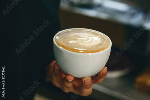 Close-up of a barista holding a cup of freshly brewed coffee in his hand.