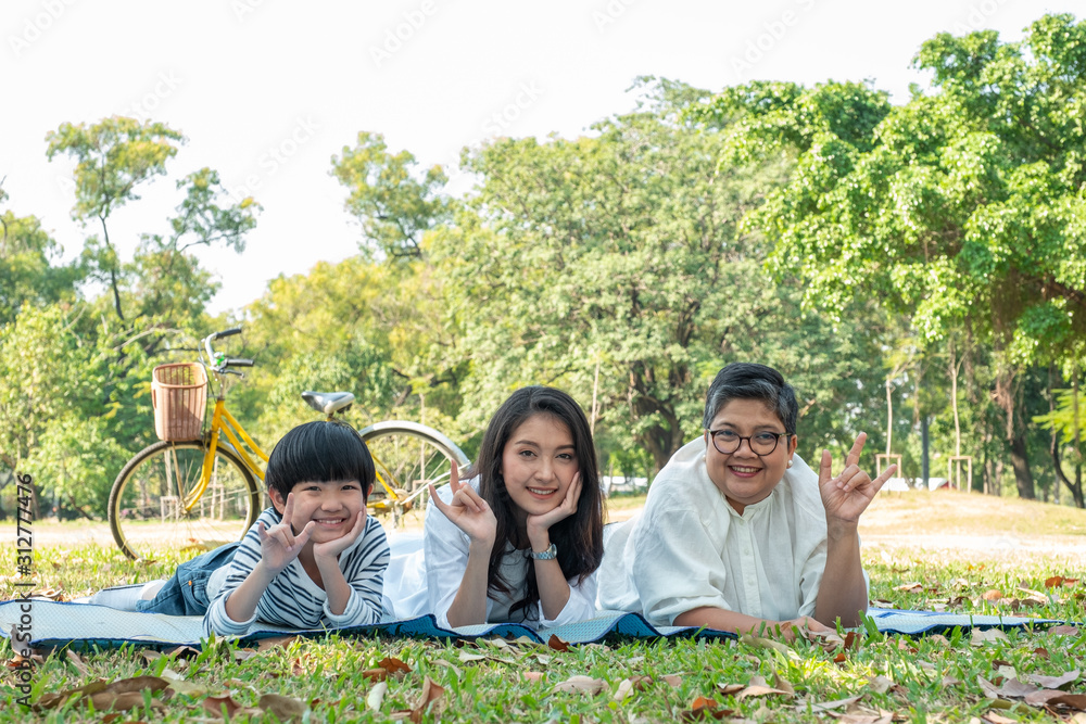 Fototapeta premium Happy family grandmother daughter and grandson laying down and doing I love you in hand sign language with smiling in park. Happy family concept