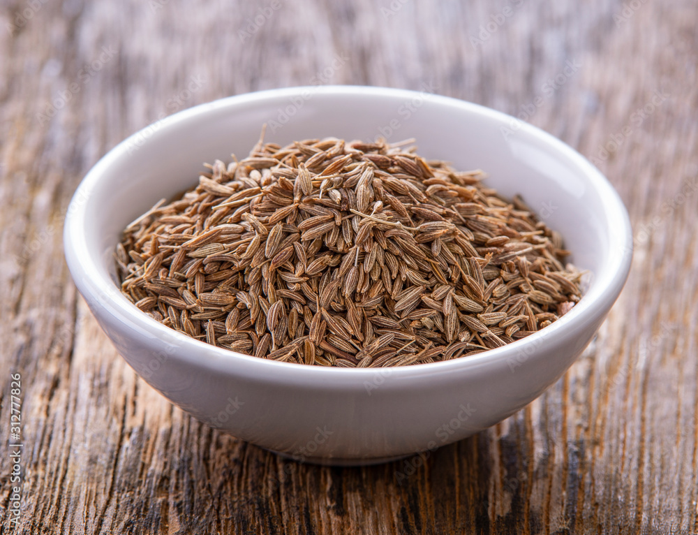 Cumin seeds in white bowl on wooden table Cumin seeds in white bowl on wooden table