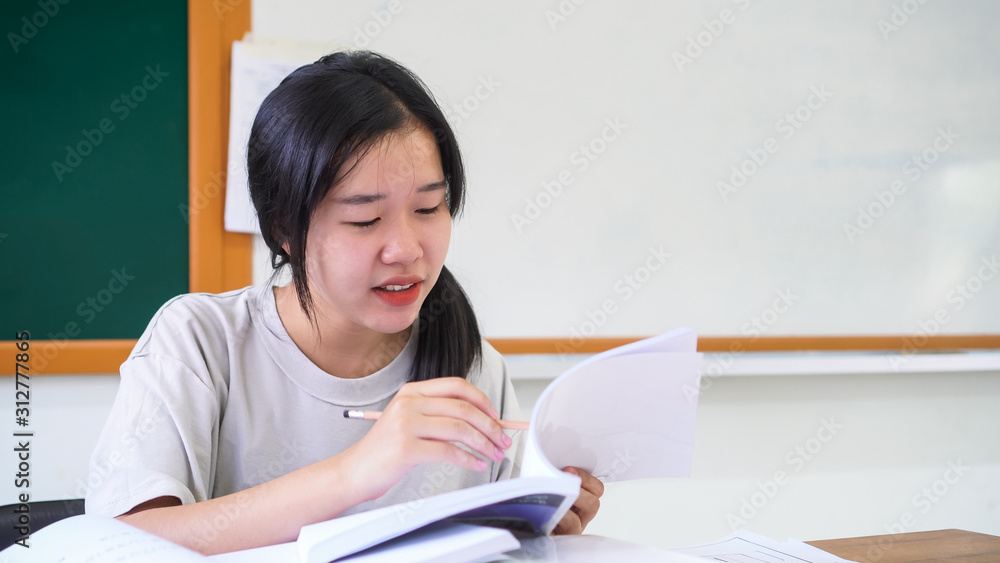 Happy teenage Asian students laughing feeling excited, so glad when doing project homework or work approved successful,sitting at front green board looking happiness in positive good with textbook Happy teenage Asian students laughing feeling excited, so glad when doing project homework or work approved successful,sitting at front green board looking happiness in positive good with textbook