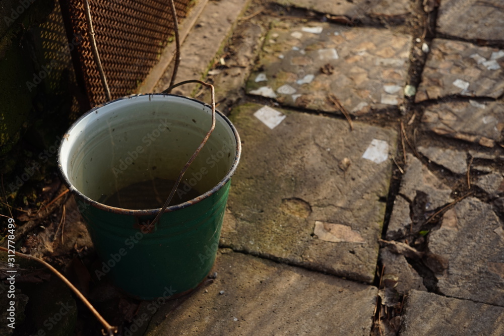 old bucket full of water with metal handle on the floor outdoor