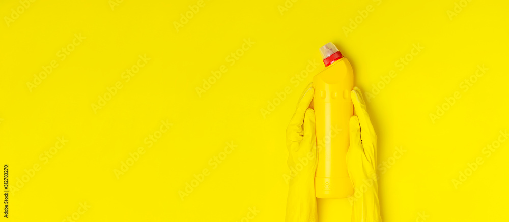 House cleaning concept. Women's hands hold household chemicals disinfectant antibacterial gel yellow rubber gloves sponge rags on yellow background. Flat lay top view copy space. Cleaning accessories