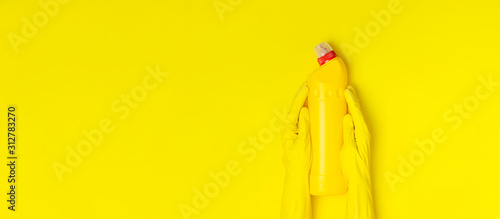 House cleaning concept. Women's hands hold household chemicals disinfectant antibacterial gel yellow rubber gloves sponge rags on yellow background. Flat lay top view copy space. Cleaning accessories