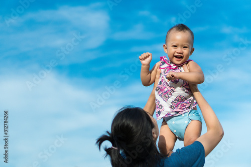 Foto Authentic family portrait: Baby is raising to the sky by her mom's arms