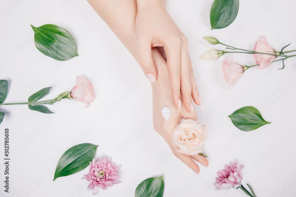 Cosmetic cream on female hands with pink flowers on white background, flat lay. Concept spa winter skin care