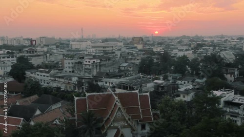 Bangkok / Thailand - July 21, 2014: Camera pans up from a downshot of a night city view with a Buddhist temple in a foreground to the twilight sky with a red sun setting down. (ID: 312786488)