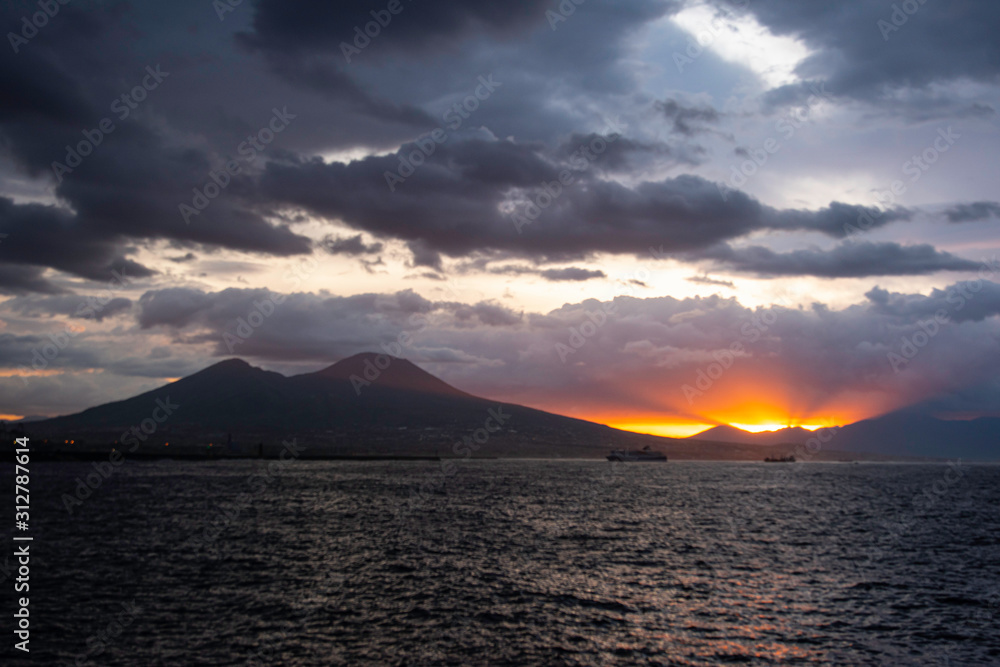 Mount Vesuvius at dawn with sun coming above the horizon with a cloudy sky.