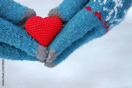 Valentine's day, red knitted heart in female hands in gloves on white snow background. Concept of romantic love, winter weather