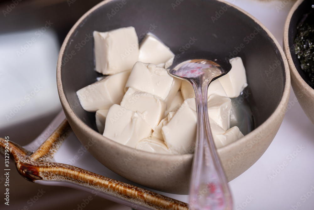 Square pieces of tofu cheese in a deep bowl with a spoon Square pieces of tofu cheese in a deep bowl with a spoon