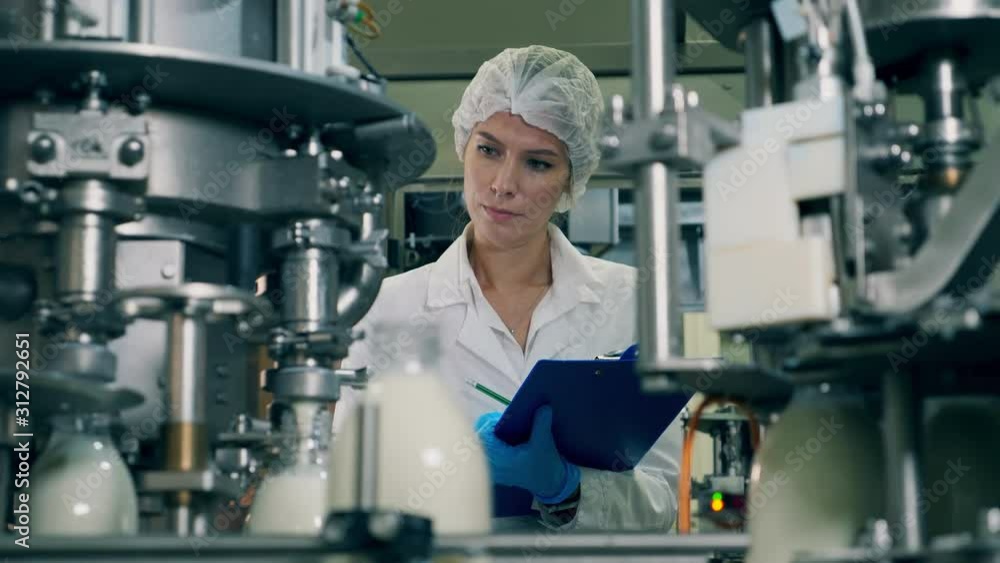 Woman checks bottles with milk on a industrial food and drinks plant conveyor. Woman checks bottles with milk on a industrial food and drinks plant conveyor.