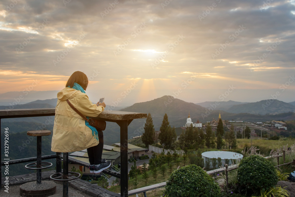 Asian traveler woman with scarf drinking a cup of espresso coffee and enjoy nature view of the mountain landscape in the morning with sunlight