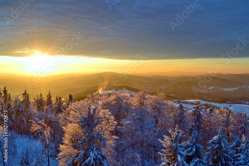 Beautiful winter sunset in Krkonose Mountains. Frozen trees, silhouettes of mountains, clouds. 