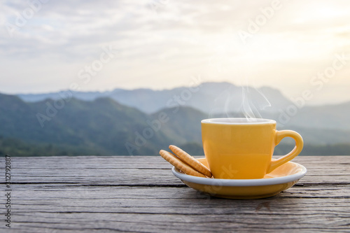 A white cup of hot espresso coffee mugs placed with cookies on a wooden floor with morning fog and moutains with sunlight background,coffee morning
