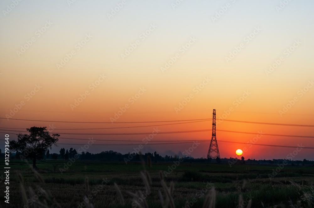 High voltage electric tower and transmission lines across the field when sunset. Electricity pylon.