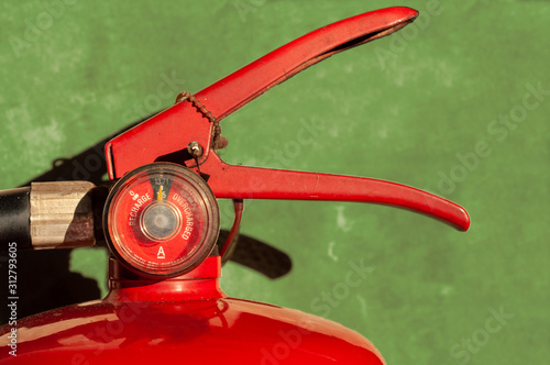 Fire extinguisher fully charged with gauge pressure on green concrete wall. Head section picture.