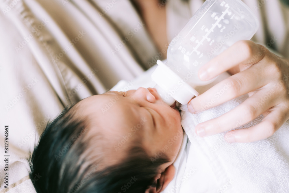 Mother feeding her adorable newborn baby kid's room at home.A woman feeds a newborn with modified milk from a bottle Mother feeding her adorable newborn baby kid's room at home.A woman feeds a newborn with modified milk from a bottle