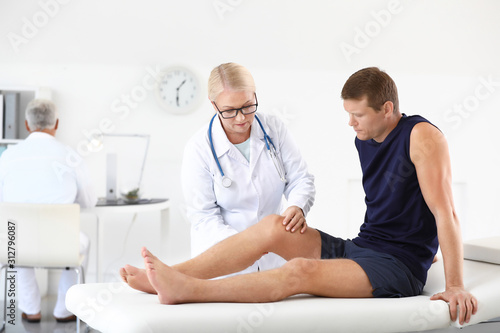 Mature doctor examining sportsman with joint pain in clinic