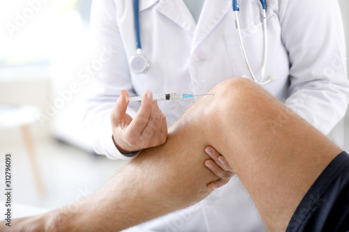 Doctor giving sportsman with joint pain injection in clinic, closeup photo